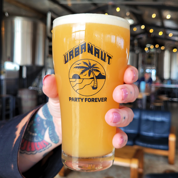 A hand holding an Urbanaut pint glass filled with delicious hazy craft beer.